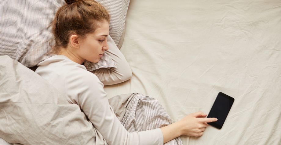 A woman lying in bed. her phone is beside her